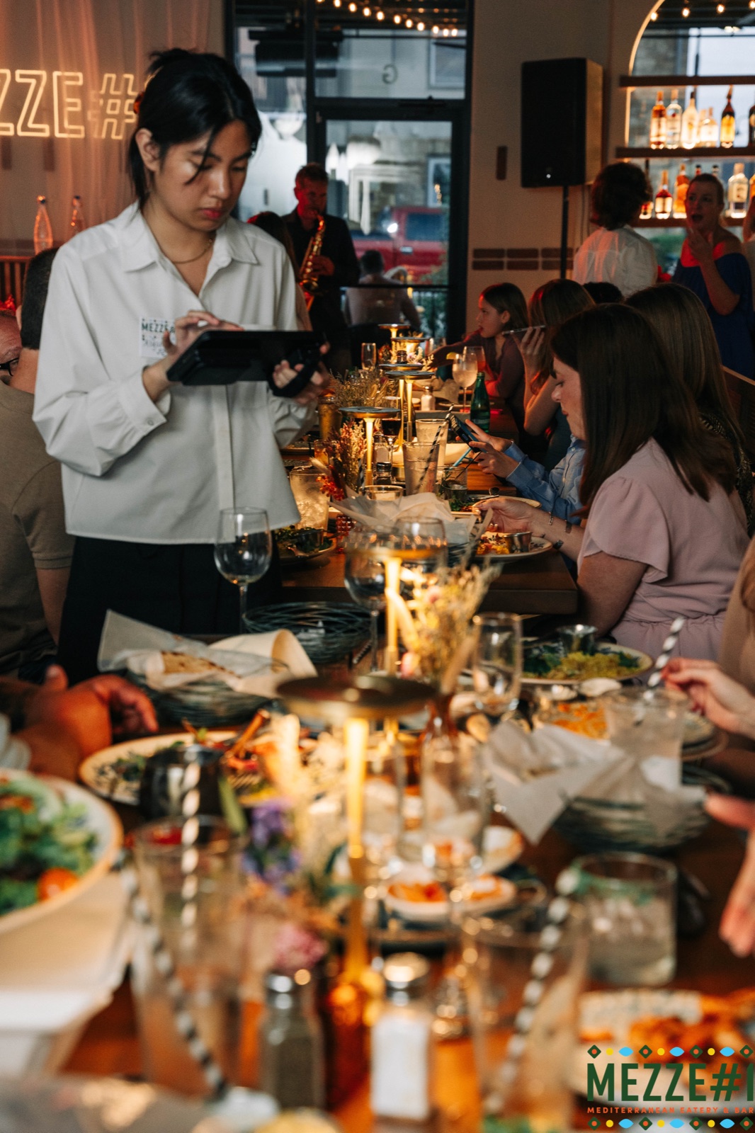 A server taking orders at a full event table, the room lit by warm chandeliers