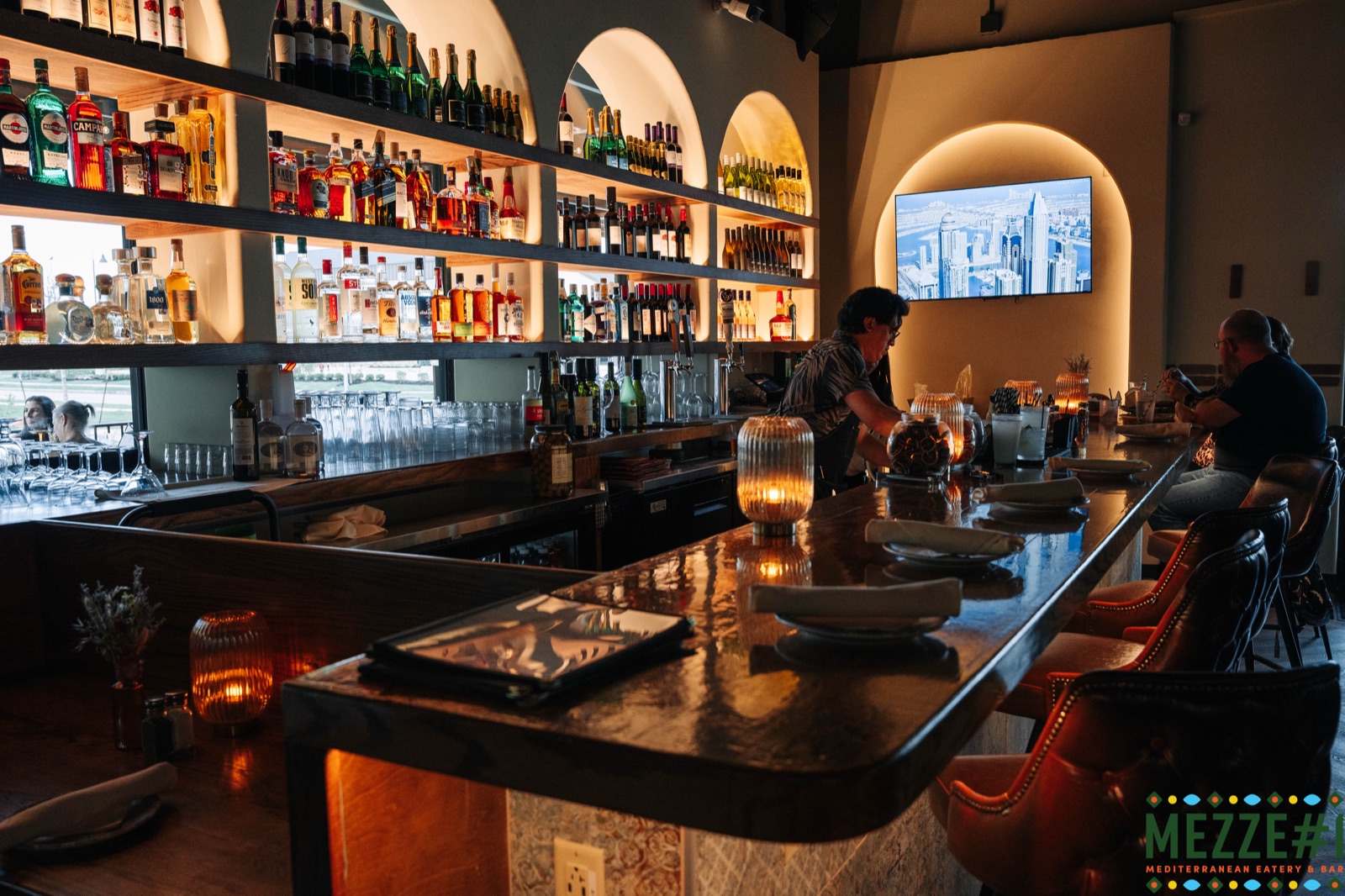 The Mezzé #1 bar — arched bottle alcoves, warm candlelight, leather barstools, and the glowing MEZZE#1 sign